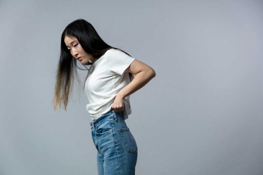 Young woman in a white shirt and jeans posing against a gray background.