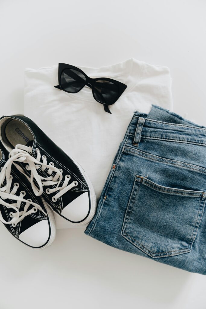 Flat lay of jeans, sneakers, and sunglasses for a modern casual style.